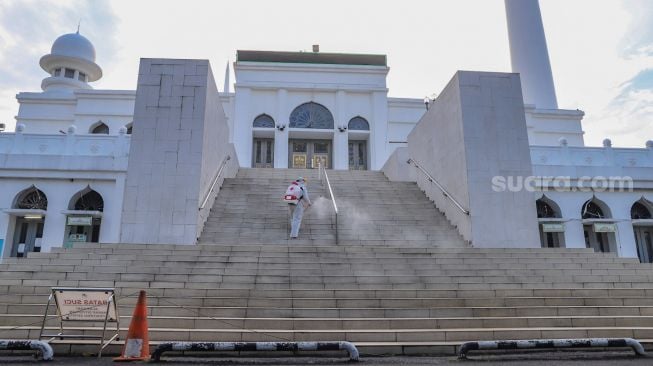 Petugas menyemprotkan cairan disinfektan area luar  Masjid Agung Al-Azhar, Jakarta Selatan, Rabu (3/6). [Suara.com/Alfian Winanto]