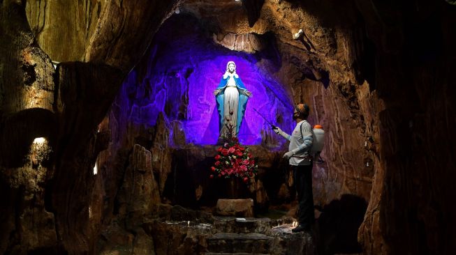 Pekerja menyemprotkan cairan disinfektan di Gua Maria di Gereja Kristus Raja, Surabaya, Jawa Timur, Jumat (5/6/2020). [ANTARA FOTO/Zabur Karuru]