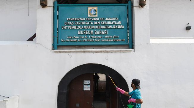 Seorang pekerja menyemprotkan cairan disinfektan pada pintu masuk Museum Bahari, Jakarta, Sabtu (6/6/2020). [ANTARA FOTO/M Risyal Hidayat]