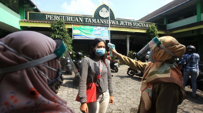 Petugas sekolah mengukur suhu tubuh orangtua/wali murid saat pengambilan surat keterangan lulus pelajar kelas IX di SMP Taman Dewasa Jetis, Yogyakarta, Senin (8/6/2020).  [ANTARA FOTO/Andreas Fitri Atmoko]