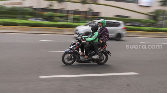 Driver ojek online membawa penumpang melintas di area Bundaran Hotel Indonesia, Jakarta, Senin (8/6).  [Suara.com/Alfian Winanto]