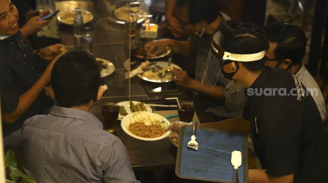 Seorang pelayan menggunakan alat pelindung wajah saat melayani pengunjung di The Atjeh Connection Resto and Coffee, Jakarta, Senin (8/6). [Suara.com/Angga Budhiyanto]