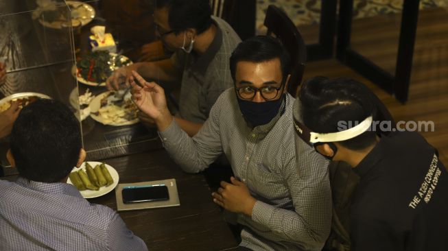 Seorang pelayan menggunakan alat pelindung wajah saat melayani pengunjung di The Atjeh Connection Resto and Coffee, Jakarta, Senin (8/6). [Suara.com/Angga Budhiyanto]