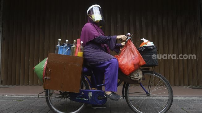 Penjual jamu keliling, Tidar dengan menggunakan masker dan pelindung wajah berpose di kawasan Pasar Baru, Jakarta, Selasa (9/6). [Suara.com/Angga Budhiyanto]