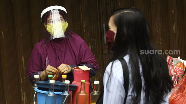 Penjual jamu keliling, Tidar dengan menggunakan masker dan pelindung wajah melayani pembeli di kawasan Pasar Baru, Jakarta, Selasa (9/6).  [Suara.com/Angga Budhiyanto]