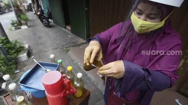 Penjual jamu keliling, Tidar dengan menggunakan masker dan pelindung wajah melayani pembeli di kawasan Pasar Baru, Jakarta, Selasa (9/6). [Suara.com/Angga Budhiyanto]