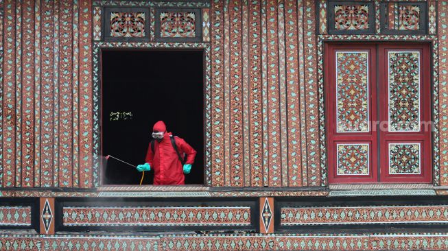 Petugas memberikan disinfektan pada bangunan rumah Gadang di Anjungan Sumatra Barat, Taman Mini Indonesia Indah, Jakarta Timur, Rabu (10/6). [Suara.com/Alfian Winanto]
