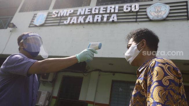 Petugas memindai suhu tubuh seorang tamu dalam simulasi pendaftaran di posko PPDB SMP Negeri 60, Kecamatan Gambir, Jakarta Pusat, Rabu (10/6). [Suara.com/Angga Budhiyanto]