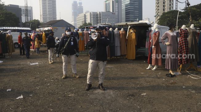 Petugas memberi imbauan kepada pedagang untuk menerapkan protokol kesehatan saat berdagang di Pasar Tasik, Jakarta, Kamis (11/6). [Suara.com/Angga Budhiyanto]