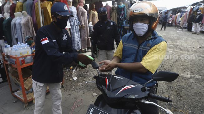 Petugas menyemprotkan cairan pembersih tangan kepada pengunjung usai mengunjungi Pasar Tasik, Jakarta, Kamis (11/6). [Suara.com/Angga Budhiyanto]