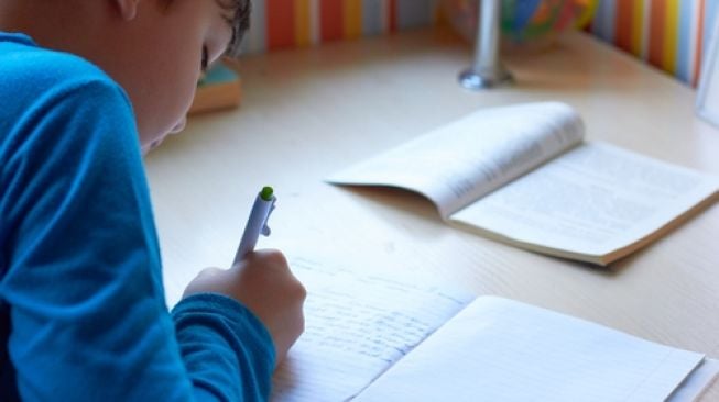 Anak menulis di buku. (Shutterstock)