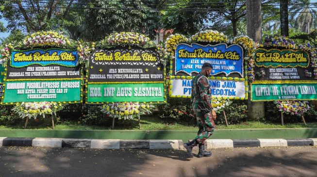 Seorang anggota TNI melintas didepan karangan bunga duka cita atas wafatnya mantan Kepala Staf TNI Angkatan Darat (KSAD) Letjen TNI Pramono Edhie Wibowo di Puri Cikeas, Bogor, Jawa Barat, Minggu (14/6). [Suara.com/Alfian Winanto]