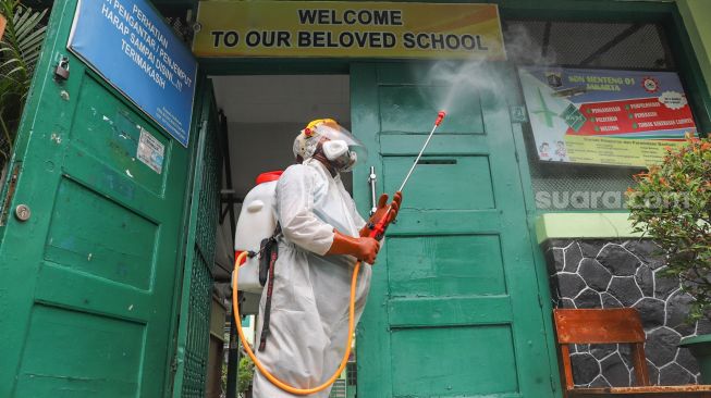 Petugas PMI menyemprotkan disingektan di pintu masuk  SDN 01 Menteng, Jakarta Pusat, Senin (15/1). [Suara.com/Alfian Winanto]