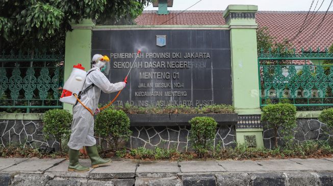 Petugas PMI menyemprotkan disinfektan area luar  SDN 01 Menteng, Jakarta Pusat, Senin (15/1). [Suara.com/Alfian Winanto]