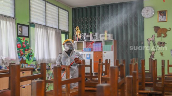 Petugas PMI membersihkan area kelas dengan disinfektan di SDN 01 Menteng, Jakarta Pusat, Senin (15/1). [Suara.com/Alfian Winanto]