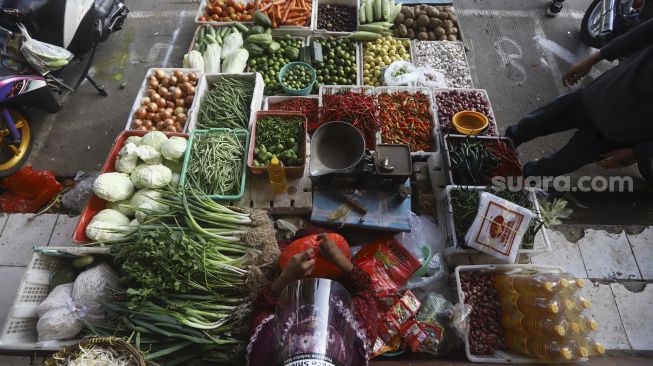 Pedagang dengan menggunakan pelindung wajah melayani pembeli di Pasar Perumnas Klender, Jakarta, Selasa (16/6). [Suara.com/Angga Budhiyanto]