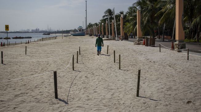 Pekerja berjalan di samping pagar pembatas yang digunakan untuk menjaga jarak pengunjung saat bermain di pantai Lagoon, Taman Impian Jaya Ancol, Jakarta, Rabu (17/6).  [ANTARA FOTO/Dhemas Reviyant]