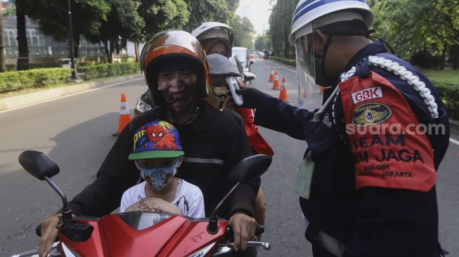 Petugas memeriksa suhu tubuh pengunjung sebelum memasuki komplek Gelora Bung Karno, Jakarta, Kamis (18/6). [Suara.com/Angga Budhiyanto]
