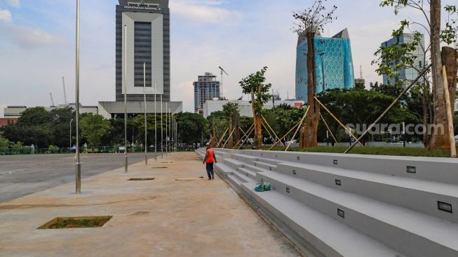 Pekerja melintas di deretan tribun tempat duduk di area revitalisasi Monas, Jakarta Pusat, Kamis (18/6). [Suara.com/Alfian Winanto]