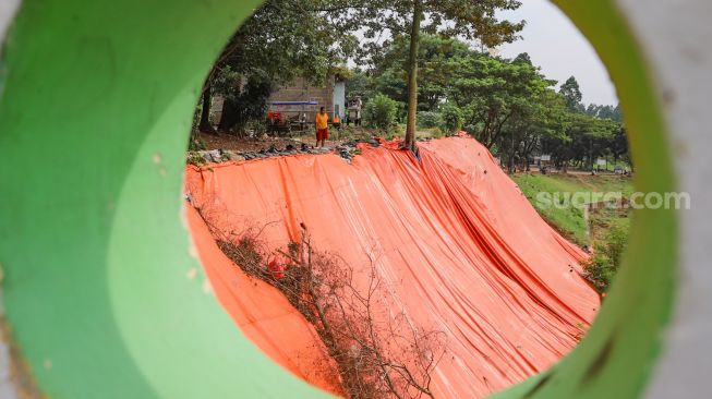 Terpal besar yang menutupi lokasi tanah longsor di pinggir Banjir Kanal Timur (BKT), Malaka Sari, Jakarta Timur, Jumat (19/6). [Suara.com/Alfian Winanto]