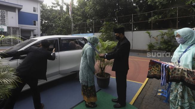 Seorang murid menerima pengalungan medali dari guru sebagai tanda wisuda kelulusan sekolah secara "Drive Thru" di Madrasah Aliyah Annajah, Ciledug Raya, Jakarta, Jumat (19/6). [Suara.com/Angga Budhiyanto]