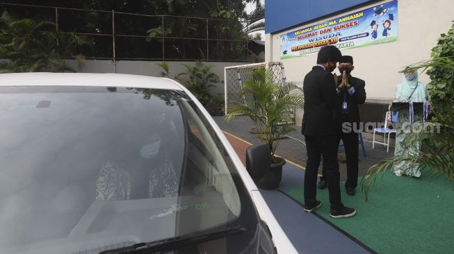 Seorang murid saat melaksanakan prosesi wisuda kelulusan sekolah secara "Drive Thru" di Madrasah Aliyah Annajah, Ciledug Raya, Jakarta, Jumat (19/6). [Suara.com/Angga Budhiyanto]