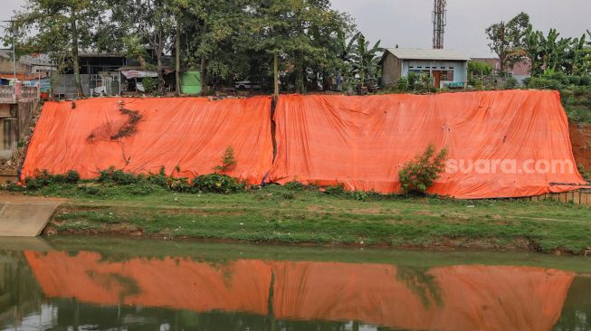 Penampakan terpal besar yang menutupi lokasi tanah longsor di pinggir Banjir Kanal Timur (KBT), Malaka Sari, Jakarta Timur, Jumat (19/6). [Suara.com/Alfian Winanto