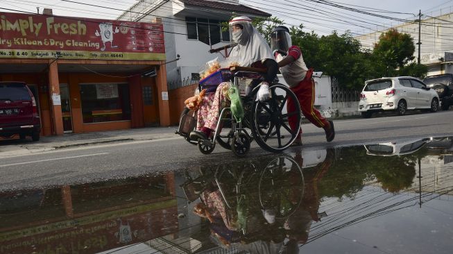 Seorang penyandang disabilitas, Yanti (34) duduk di atas kursi roda dan didorong anaknya saat berjualan makanan di jalanan Kota Pekanbaru, Riau, Sabtu (20/6). [ANTARA FOTO/FB Anggoro]