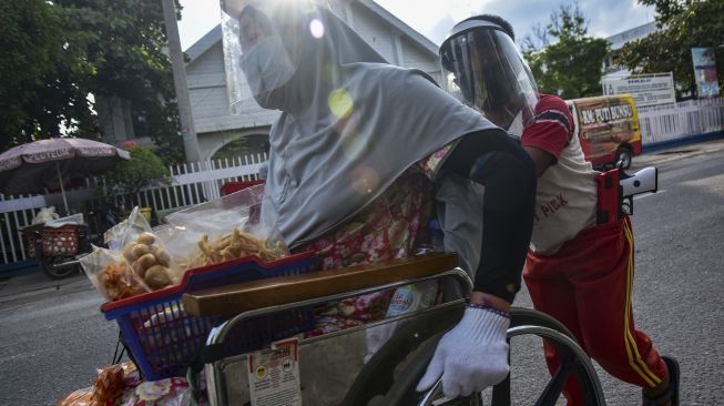 Seorang penyandang disabilitas, Yanti (34) duduk di atas kursi roda dan didorong anaknya saat berjualan makanan di jalanan Kota Pekanbaru, Riau, Sabtu (20/6). [ANTARA FOTO/FB Anggoro