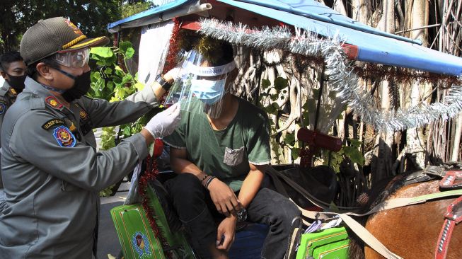 Anggota Satpol PP Kota Bogor membagikan alat pelindung wajah (Face Shield) dan masker untuk pengemudi delman di jalan Juanda, Kota Bogor, Jawa Barat, Minggu (21/6). [ANTARA FOTO/Arif Firmansyah]