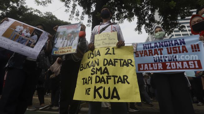 Sejumlah orang tua siswa yang tergabung dalam Gerakan Emak-Bapak Peduli Keadilan dan Pendidikan (Geprak) membentangkan poster saat melakukan aksi unjuk rasa di depan Balai Kota DKI Jakarta, Selasa (23/6). [Suara.com/Angga Budhiyanto]