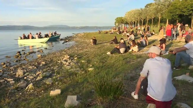 Para musisi Italia coba menghibur penonton dengan cara memainkan musik di pinggir danau Trasimeno dengan menaiki perahu milik nelayan. (tangkapan layar video Reuters).