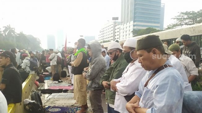 Para pendemo tolak RUU HIP salah Asar berjemaah di jalan depan gedung DPR saat turun hujan. (Suara.com/Arga)