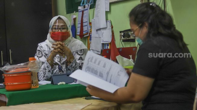 Orang tua murid mengecek rapor anaknya di SDN 01 Menteng, Jakarta Pusat, Kamis (25/6). [Suara.com/Alfian Winanto]