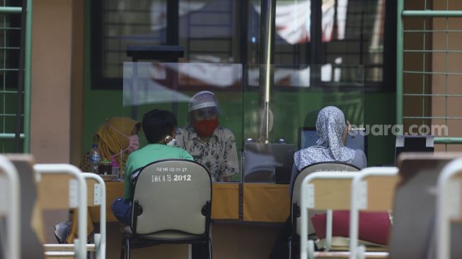 Petugas melayani orang tua siswa dan calon siswa di posko Penerimaan Peserta Didik Baru (PPDB) di SMK Negeri 15, Jakarta, Kamis (25/6). [Suara.com/Angga Budhiyanto]