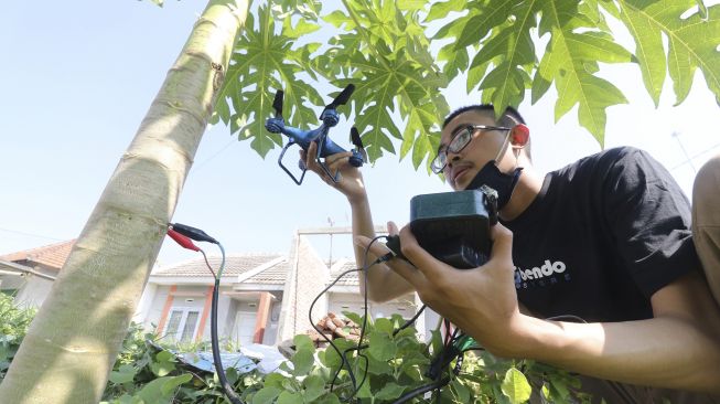 Pelajar Madrasah Aliyah Negeri 2 Kota Kediri, Muhammad Azhar Syahruddin melakukan pengisian daya baterai pesawat nirawak (drone) buatannya di pohon pepaya di Desa Bendo, Kediri, Jawa Timur, Sabtu (27/6). [ANTARA FOTO/Prasetia Fauzani]