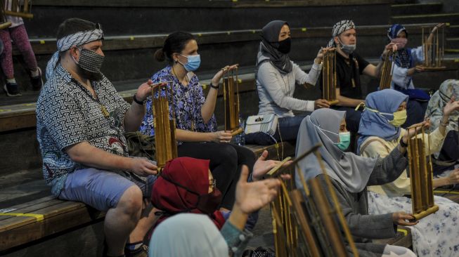 Wisatawan domestik dan mancanegara memainkan angklung sambil duduk berjaga jarak fisik di Saung Angklung Udjo, Bandung, Jawa Barat, Sabtu (27/6). [ANTARA FOTO/Raisan Al Farisi]