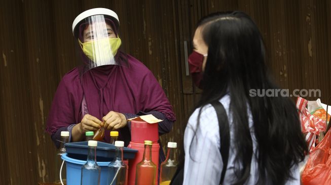 Penjual jamu keliling, Tidar (46) dengan menggunakan masker dan pelindung wajah melayani pembeli di kawasan Pasar Baru, Jakarta, Selasa (9/6). [Suara.com/Angga Budhiyanto]