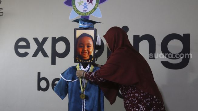 Kepala Sekolah mengalungkan piagam tanda kelulusan kepada siswa Kelompok Bermain Taman Kanak-kanak (KB TK) saat wisuda virtual menggunakan Roboda (Robot Wisuda) di Sekolah Nasional Satu (Nassa School), Bekasi, Jawa Barat, Rabu (1/7) . [Suara.com/Angga Budhiyanto]
