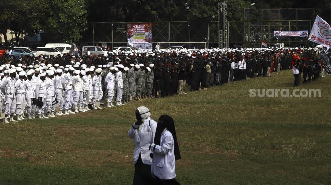 Dua massa melintas saat sejumlah massa dari berbagai elemen organisasi kemasyarakatan Islam menggelar 'Apel Siaga Ganyang Komunis' di Lapangan Ahmad Yani, Kebayoran Lama, Jakarta Selatan, Minggu (5/7). [Suara.com/Angga Budhiyanto]