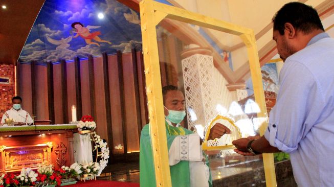 Seorang pastor dengan menggunakan masker dan pembatas membagikan hosti atau tubuh dan darah kristus kepada umat Katolik yang melaksanakan ibadah hari Minggu di gereja Santo Gregorius Agung Oeleta di Kota Kupang, NTT,Minggu (5/7). [ANTARA FOTO/Kornelis Kaha]