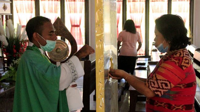 Seorang pastor dengan menggunakan masker dan pembatas membagikan hosti atau tubuh dan darah kristus kepada umat Katolik yang melaksanakan ibadah hari Minggu di gereja Santo Gregorius Agung Oeleta di Kota Kupang, NTT,Minggu (5/7). [ANTARA FOTO/Kornelis Kaha]