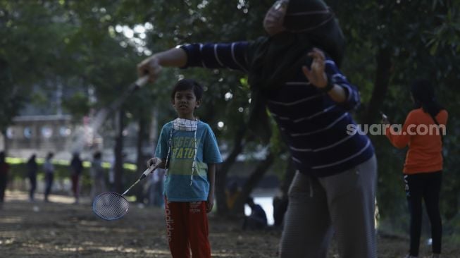 Dua anak bermain bulutangkis saat Hari Bebas Kendaraan Bermotor (HBKB) atau Car Free Day (CFD) di kawasan Banjir Kanal Timur (BKT), Duren Sawit, Jakarta, Minggu (5/7). [Suara.com/Angga Budhiyanto] 