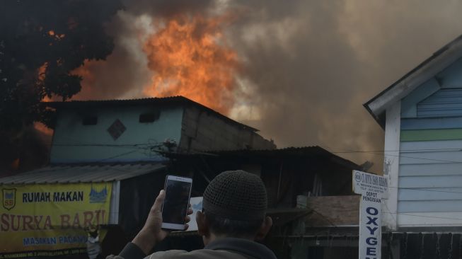 Warga mengambil gambar proses pemadaman api yang membakar sejumlah toko di Jalan Minangkabau Barat, Manggarai, Jakarta, Selasa (7/7/2020).  [ANTARA FOTO/Galih Pradipta]