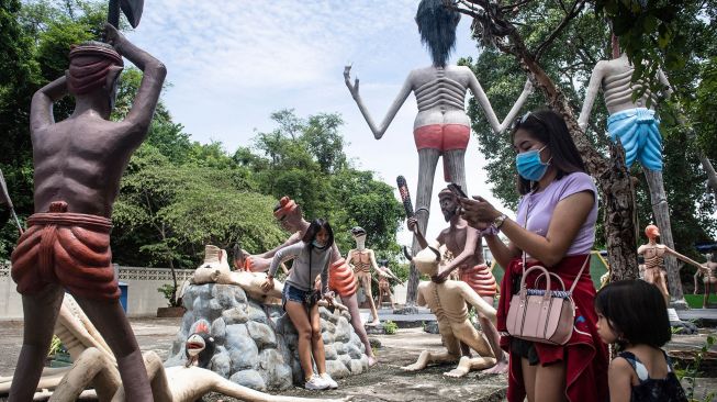 Para pengunjung mengambil foto di depan patung-patung yang menggambarkan nasib orang-orang yang tidak menjujung tinggi lima ajaran Budhha di sebuah taman yang menggambrakan neraka versi Budhha di Kuil Wat Saeng Suk di Provinsi pantai Thailand Chonburi (9/7/2020). [Lillian SUWANRUMPHA / AFP]