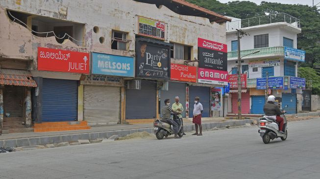 Warga berdiri di depan toko-toko yang tutup saat pemberlakuan lockdown di Bangolore, India, Rabu (15/7).  [Manjunath Kiran/AFP]