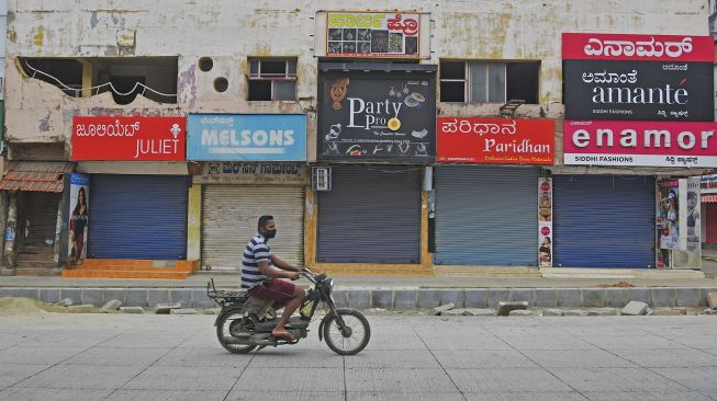 Seorang pria mengendarai sepeda motor di depan toko-toko yang tutup saat pemberlakuan lockdown di Bangolore, India, Rabu (15/7). [Manjunath Kiran/AFP]