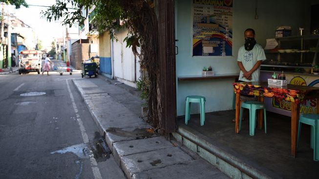 Seorang warga yang mengenakan masker wajah berdiri di dalam sebuah restoran ketika menunggu pelanggan di sepanjang jalan yang hampir kosong di Navotas di pinggiran kota Manila, Filipina, Kamis (16/7). [Ted ALJIBE / AFP]