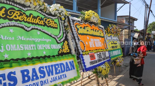 Pelayat melintas didepan karangan bunga untuk komedian Omas Wati di Rumah Duka, Cimanggis, Depok, Jawa Barat, Jumat (17/7). [Suara.com/Alfian Winanto]