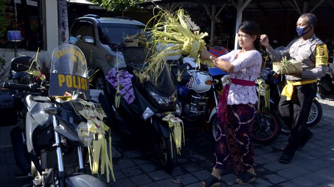 Umat Hindu dan petugas kepolisian memercikkan air suci ke kendaraan saat rangkaian persembahyangan Hari Raya Tumpek Landep di Polsek Denpasar Selatan, Bali, Sabtu (18/7/2020). [ANTARA FOTO/Fikri Yusuf]